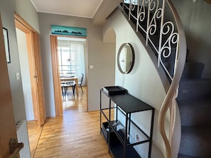 A hallway with wooden flooring, a dining area with a table and chairs, a black console table, a round mirror, and a staircase with a metal railing. - Family friendly house centrally located in Reykjavik (Reykjavík)