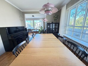 A dining area with a long wooden table, black chairs, a black piano, and large windows with a view of trees. - Family friendly house centrally located in Reykjavik (Reykjavík)