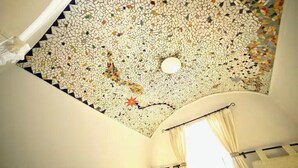 Een kamer met een plafond met een mozaïekpatroon, een bed met een wit hoofdeinde, en een raam met gordijnen.