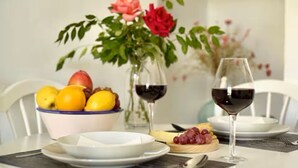 Een eettafel met een schaal fruit, twee wijnglazen en een bord kaas en druiven.