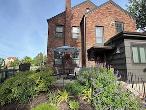 A brick building with a patio area, outdoor seating, and a garden with various plants and flowers.