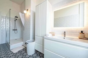 A modern bathroom with a glass shower enclosure, white tiled walls, a large mirror, and a white sink with a wooden soap dispenser. - Luxurious 130sqm apt gambetta square with AC (Carcassonne)
