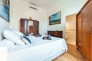 A bedroom with a bed, a wardrobe, a painting, and a bathroom visible in the background. - Elegant 130sqm AC Apt Square Gambetta (Carcassonne)