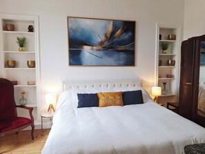 Une chambre d’hôtel bien aménagée, avec un grand lit, un fauteuil rouge, un plancher en bois et un tableau accroché au mur.