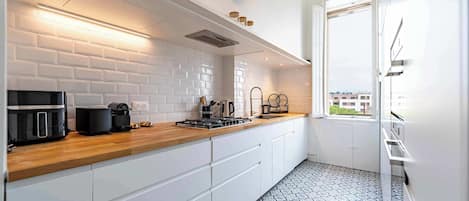 Une cuisine moderne avec des carreaux de céramique blancs disposés en motif métro, un plan de travail en bois et une vue sur les bâtiments environnants.