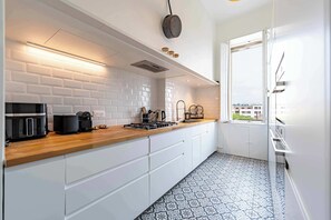 A modern kitchen with white subway tiles, a wooden countertop, and a view of buildings outside. - Elegant 130sqm AC Apt Square Gambetta (Carcassonne)