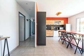A modern kitchen with a dining area, featuring a kitchen island, wooden cabinets, and a refrigerator.