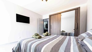 Quarto moderno com cama, um espelho grande, guarda-roupa e televisão de tela plana fixada na parede.