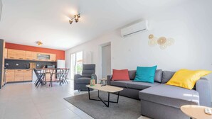 Uma sala de estar moderna com um sofá cinzento, uma mesa de centro e uma área de jantar com uma mesa e cadeiras.