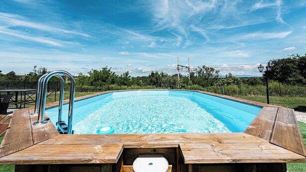 Piscina com deck de madeira e escada de metal, cercada por vegetação.