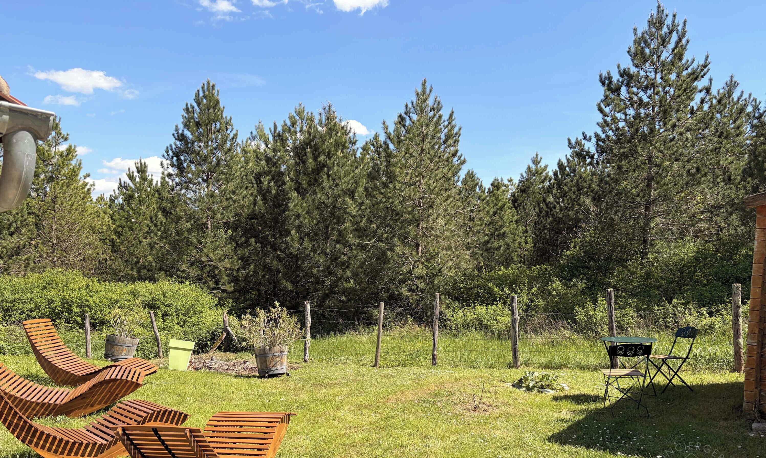 Un espacio al aire libre con césped, sillas de madera para relajarse, una mesa y sillas, y una cerca de metal.