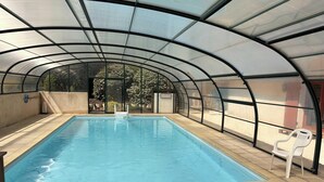 An indoor swimming pool with a glass ceiling, clear view outside, and a single white chair. - Charming countryside residence, swimming pool (Allemans)