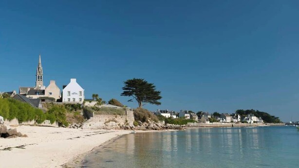 En kuststad med en framträdande kyrka, en sandstrand och ett lugnt hav.