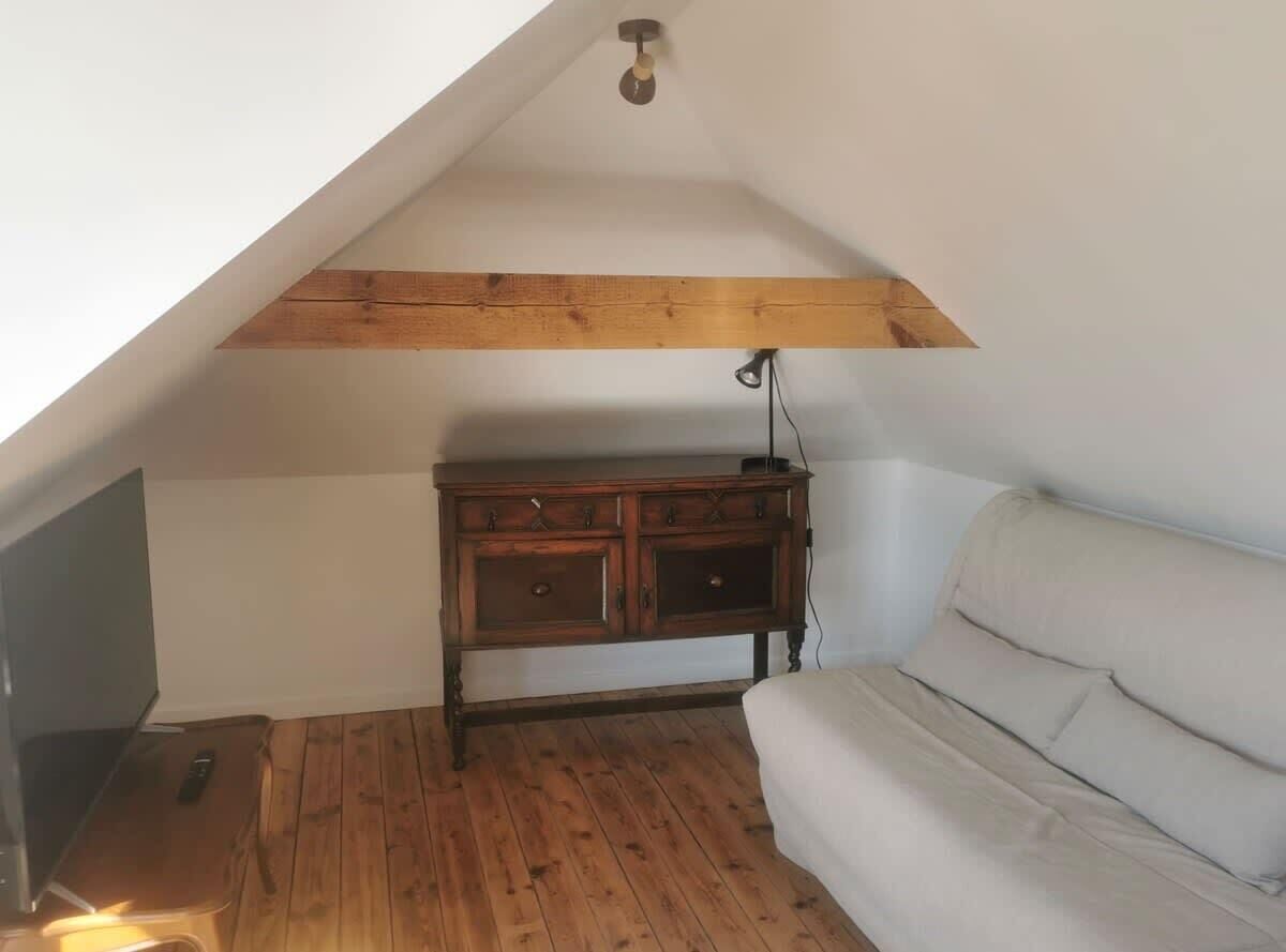 A loft bedroom with a sloped ceiling, wooden beams, a white sofa, and a wooden dresser.