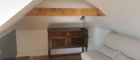 A loft bedroom with a sloped ceiling, wooden beams, a white sofa, and a wooden dresser.
