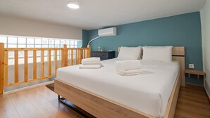 Een slaapkamer met een houten bed, wit beddengoed, een nachtkastje en een raam met uitzicht.