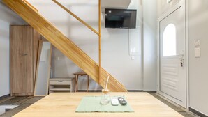 Een kamer met een houten tafel, een aan de muur bevestigde televisie, een kledingkast en een deur met een raam.