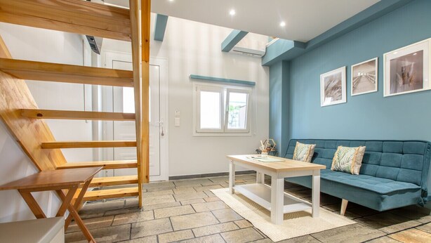 Een kamer met een houten stoel, een tafel, een blauwe bank en een raam met uitzicht.