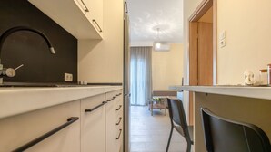 A modern kitchen with white cabinets, a black faucet, and a dining area with a table and chairs. - Bella Home by RentalsPro - Nea Plagia Halkidiki (Nea Plagia)
