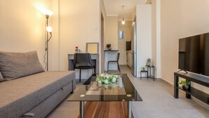 A modern living room with a sofa, a glass coffee table, a TV, and a kitchen area in the background. - Bella Home by RentalsPro - Nea Plagia Halkidiki (Nea Plagia)