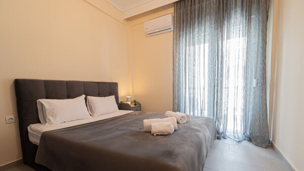A hotel room with a bed, a nightstand, a lamp, and a window with curtains. - Bella Home by RentalsPro - Nea Plagia Halkidiki (Nea Plagia)