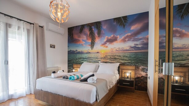A bedroom with a bed, a nightstand, a wall mural, and a door. - Stone Vista by RentalsPro - Nea Poidaia Halkidiki (Nea Poteidaia)