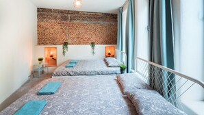Une chambre avec deux lits, un mur en briques, un luminaire suspendu et une fenêtre avec des rideaux.
