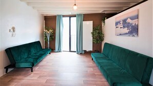 Un salon avec deux canapés verts, un plancher en bois, un luminaire suspendu, un radiateur et un tableau accroché au mur.