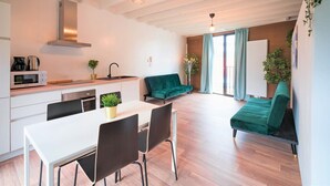 Une cuisine moderne équipée d’un four à micro-ondes, d’une cuisinière et d’un évier, un coin repas avec une table et des chaises, et un canapé vert dans un salon agrémenté d’une grande fenêtre.
