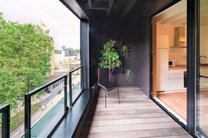 A balcony with a wooden floor, a chair, a potted plant, and a view of a street and buildings. - The Industrial Apartments 2bbk Non smk (Antwerp)