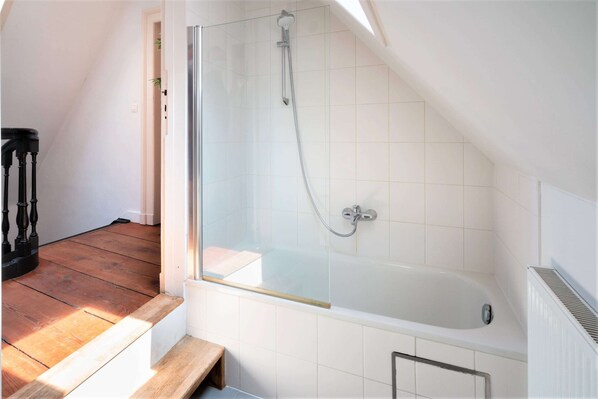 Un baño moderno con ducha de vidrio, una bañera blanca y una escalera de madera.