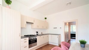 A modern kitchen with white cabinets, a stove, and a dining area with pink chairs. - Antwerp Old Town Apartment (Antwerp)
