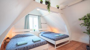 A room with two beds, a window with curtains, a small table with a lamp, and a potted plant. - Antwerp Old Town Apartment (Antwerp)