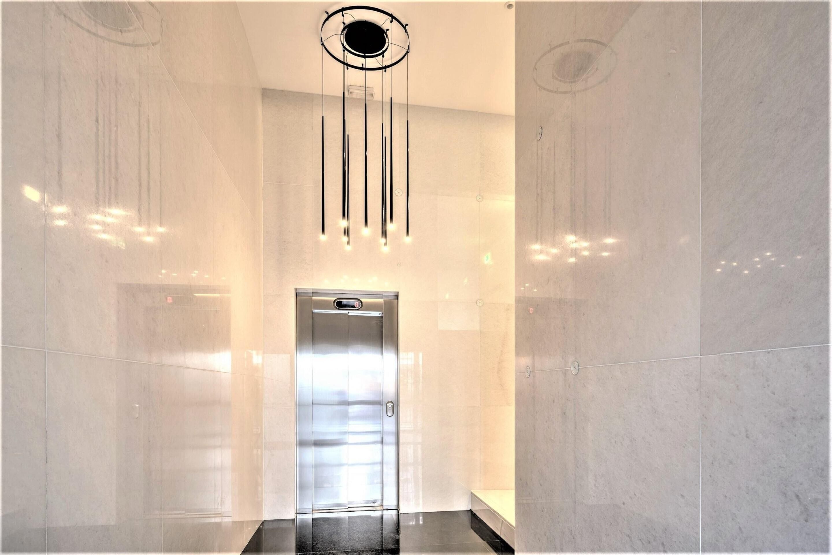 A modern elevator in a hallway with reflective marble walls and a ceiling light fixture.