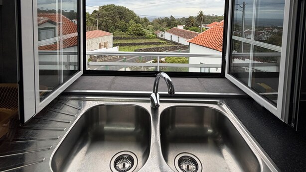 Cucina con due lavelli in acciaio inossidabile e vista su una zona residenziale tramite ampie vetrate.