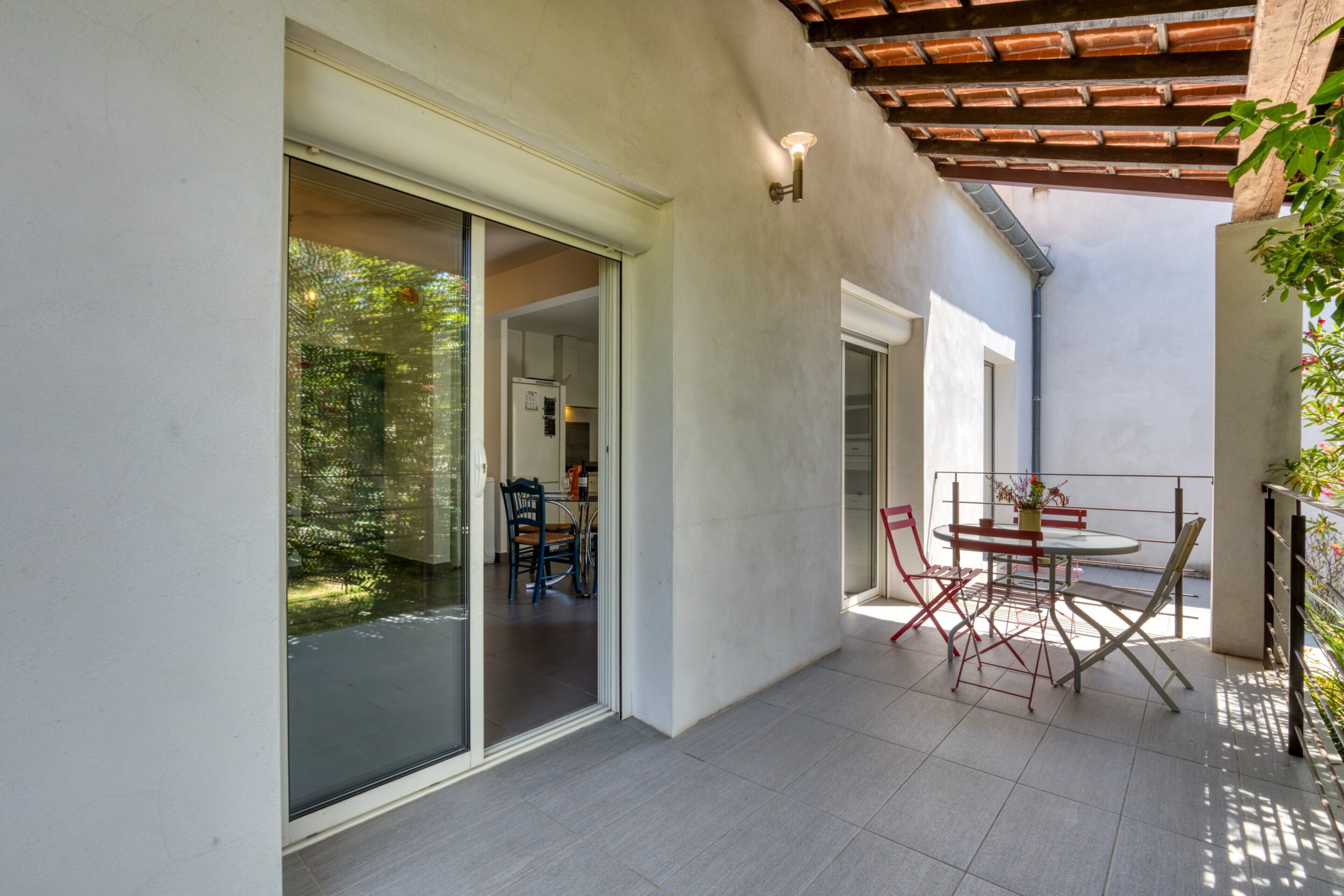 Eine moderne Terrasse mit Tisch und Stühlen, eine Glastür zum Garten und eine Pergola.
