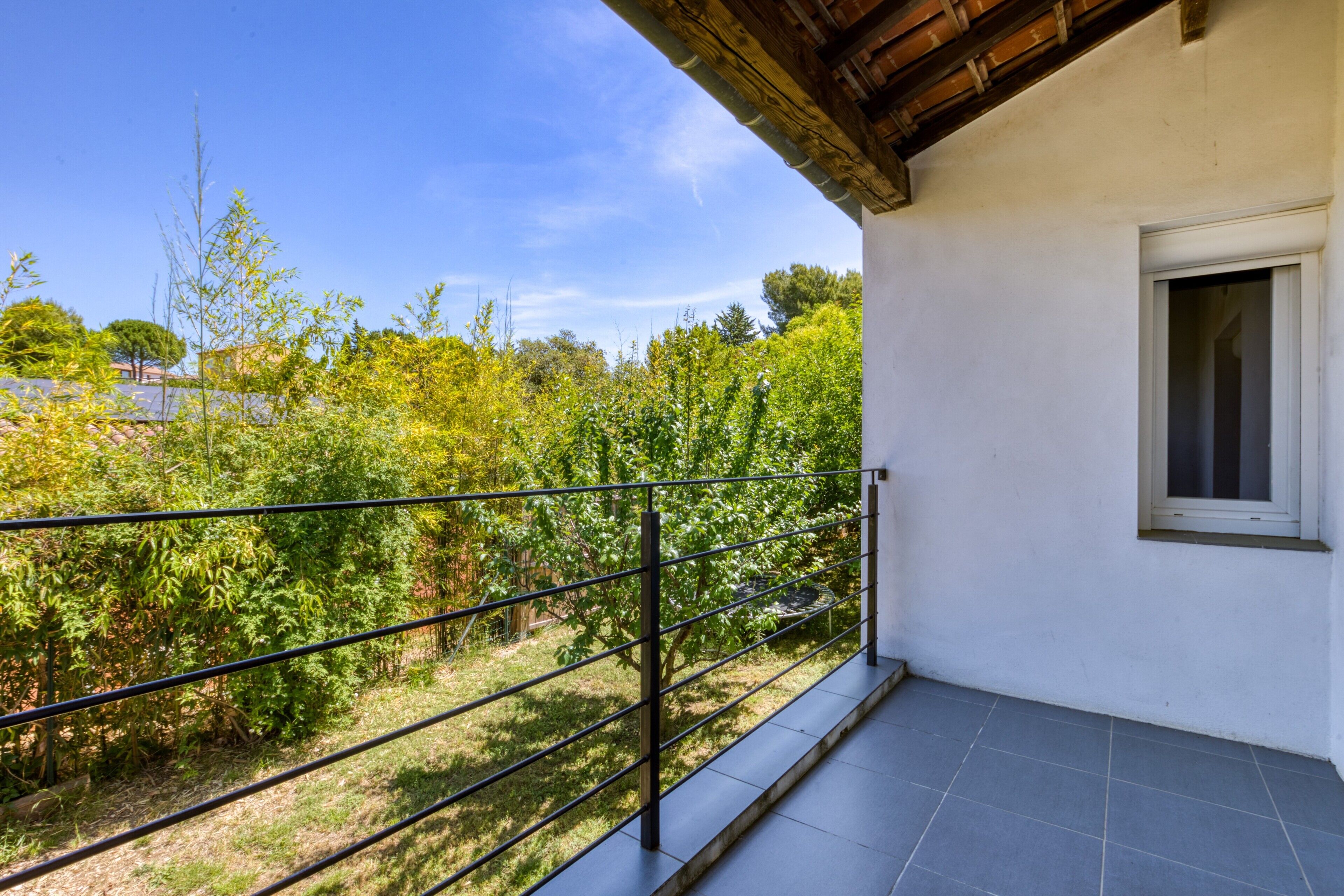 Un balcon avec une balustrade en métal, un mur blanc et une fenêtre.