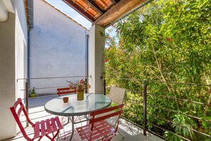 Un balcon avec une table ronde en verre, des chaises en métal rouge et une plante en pot.