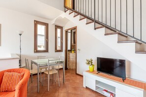 Uma sala de estar com uma mesa de jantar, cadeiras, um sofá, uma televisão em um suporte e uma escada.