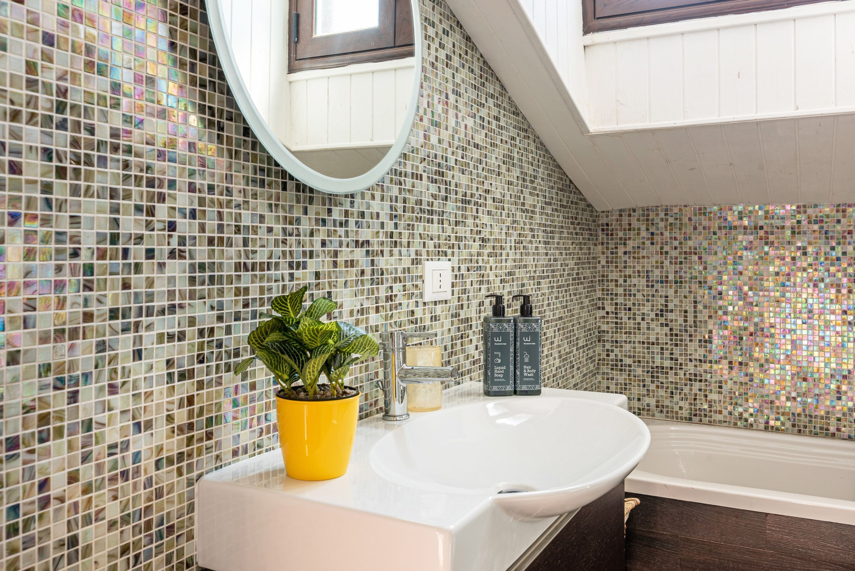 A bathroom with a white sink, a mirror, a potted plant, and a bathtub.