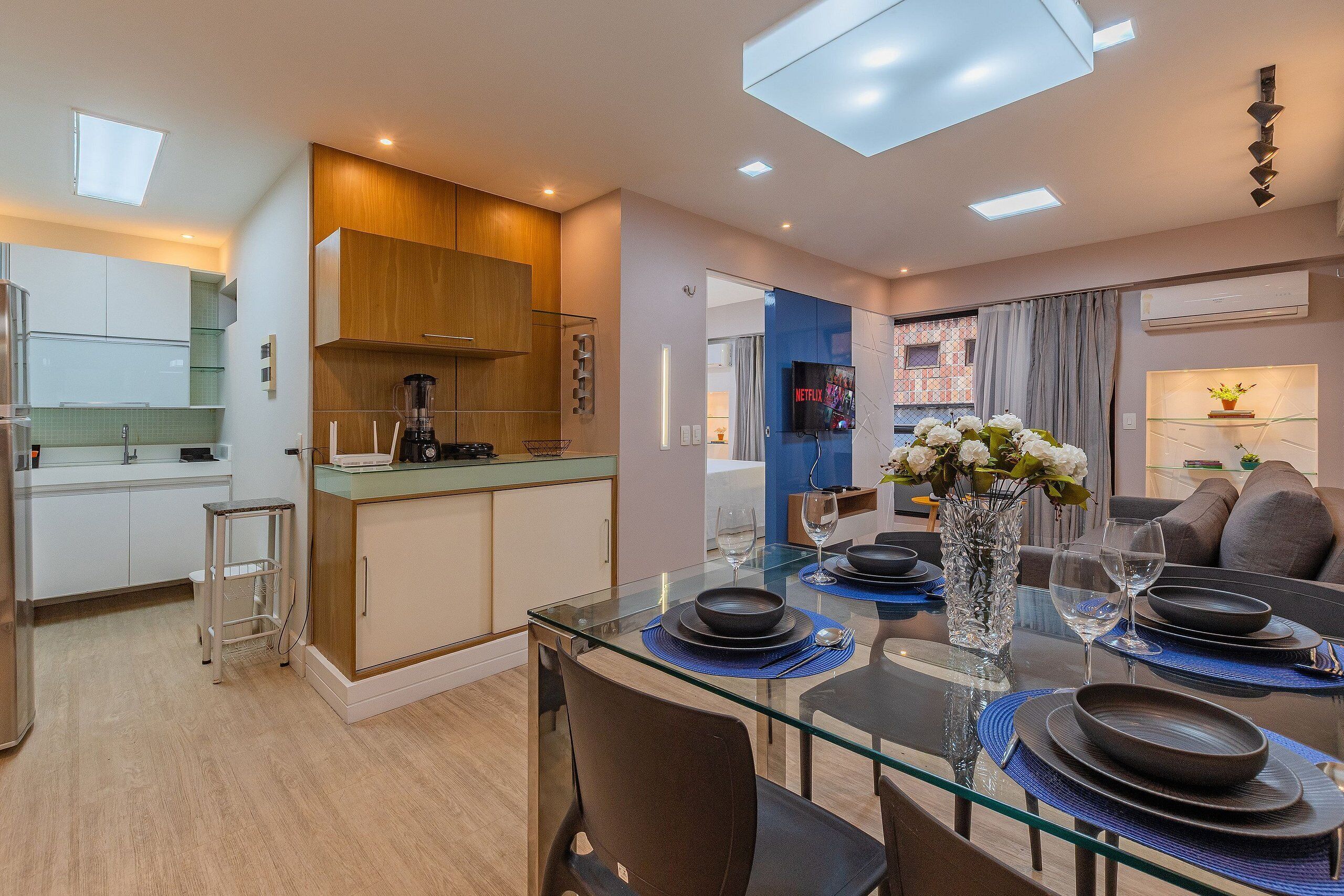A modern kitchen with a built-in stove, a dining area with a glass table, and a living room with a TV.