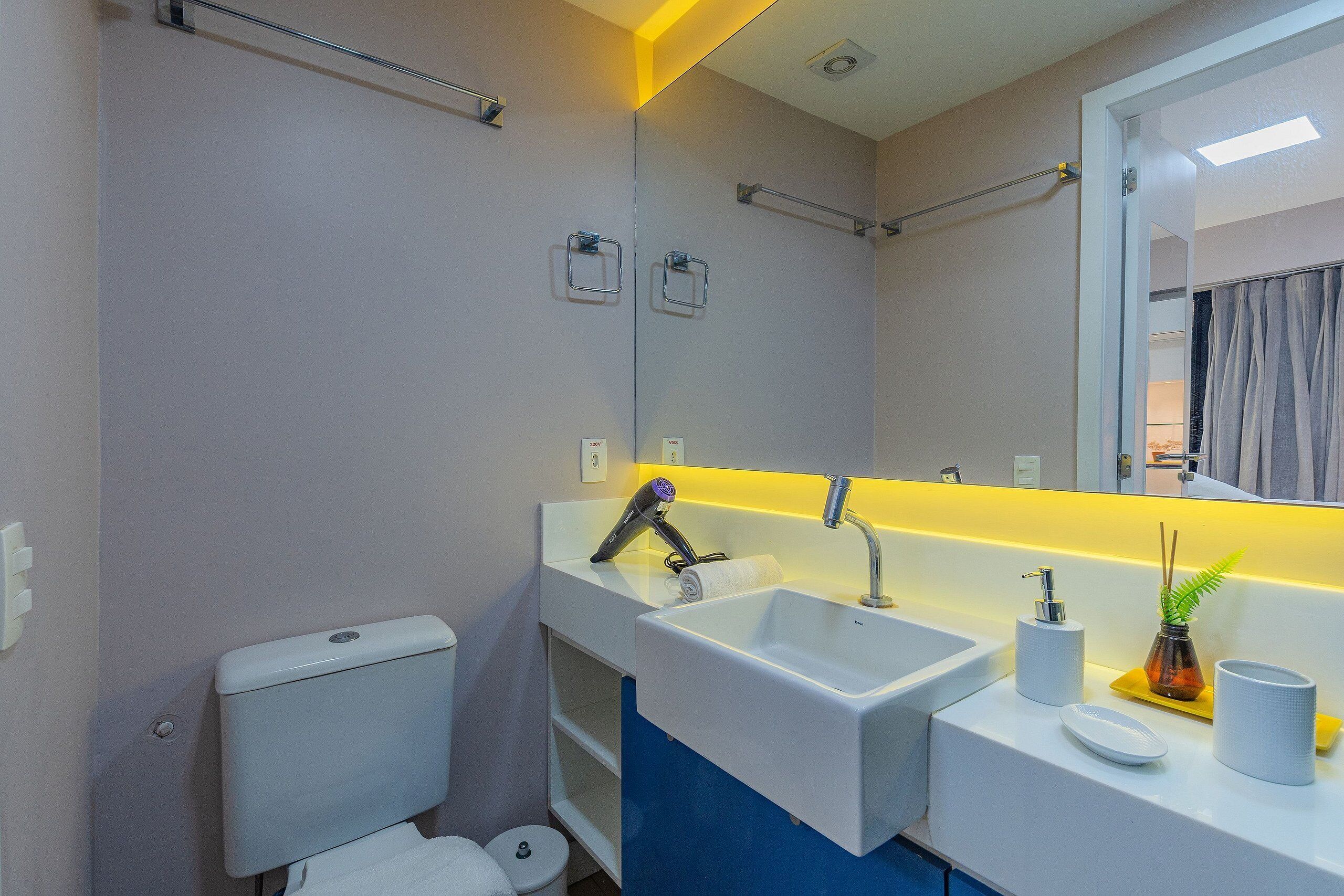 Une salle de bain équipée de toilettes, d’un lavabo, d’un miroir et d’un porte-serviettes.