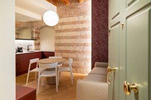 Eine moderne Küche mit Backsteinwand, einem Essbereich mit rundem Tisch und weißen Stühlen sowie einer grünen Tür mit Messinggriffen.