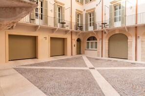 Ein Innenhof mit Fliesenboden, einer Steinsitzbank und einem Gebäude mit mehreren Türen und Fenstern.