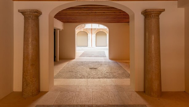 Een interieurcorridor met een houten plafond, stenen zuilen en een uitzicht door een gewelfde doorgang.