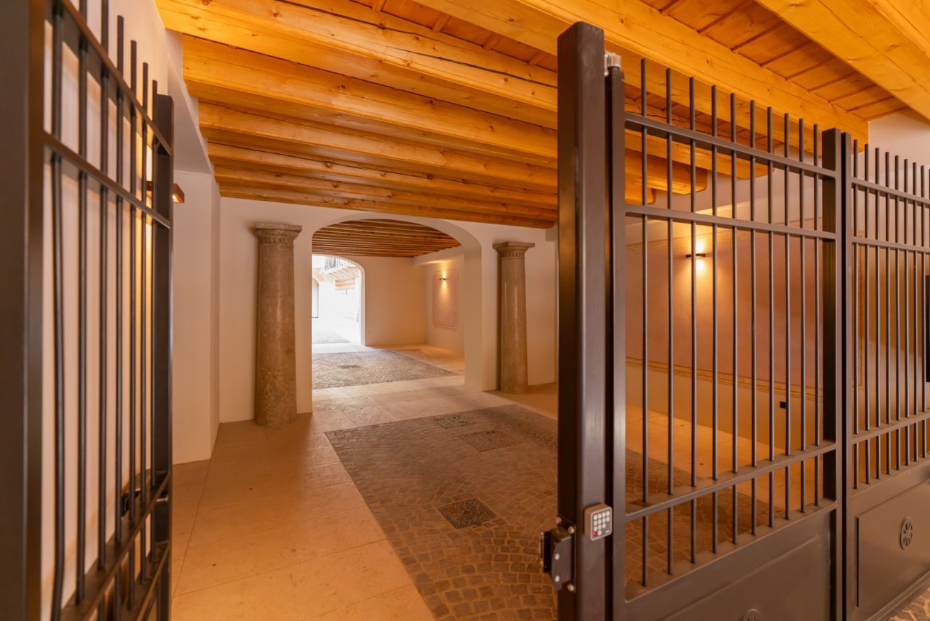 A hallway with a wooden ceiling, stone columns, and a metal gate.