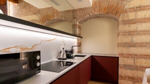Een compacte keuken met een moderne magnetron, waterkoker en spoelbak, tegen een bakstenen muur met een gewelfde plafond.