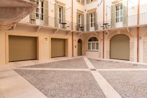 Ein Innenhof mit Fliesenboden, einer Steinsitzbank und einem Gebäude mit mehreren Türen und Fenstern.