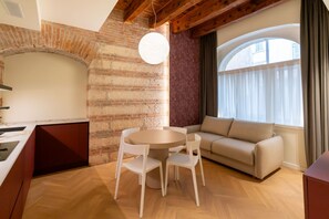 A modern living room with a brick wall, a round table with chairs, a sofa, and a large window with curtains. - Residence Le chiavi di San Pietro, 50 m from the Arena - Domus Verona   (Verona)