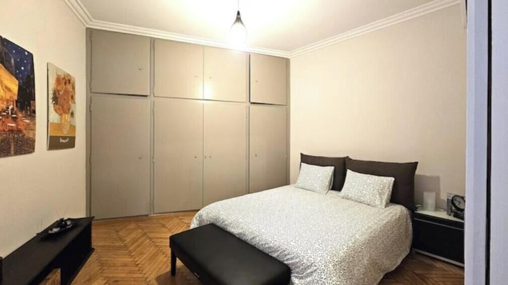 Ein Schlafzimmer mit einem Bett, einer Bank, einem Nachttisch, einem Kleiderschrank und Wandbildern.